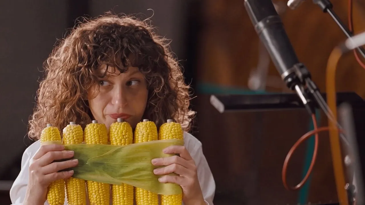 A woman holding a bundle of corn cobs beside studio microphones.