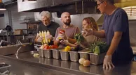 Four people preparing vegetables in a commercial kitchen.