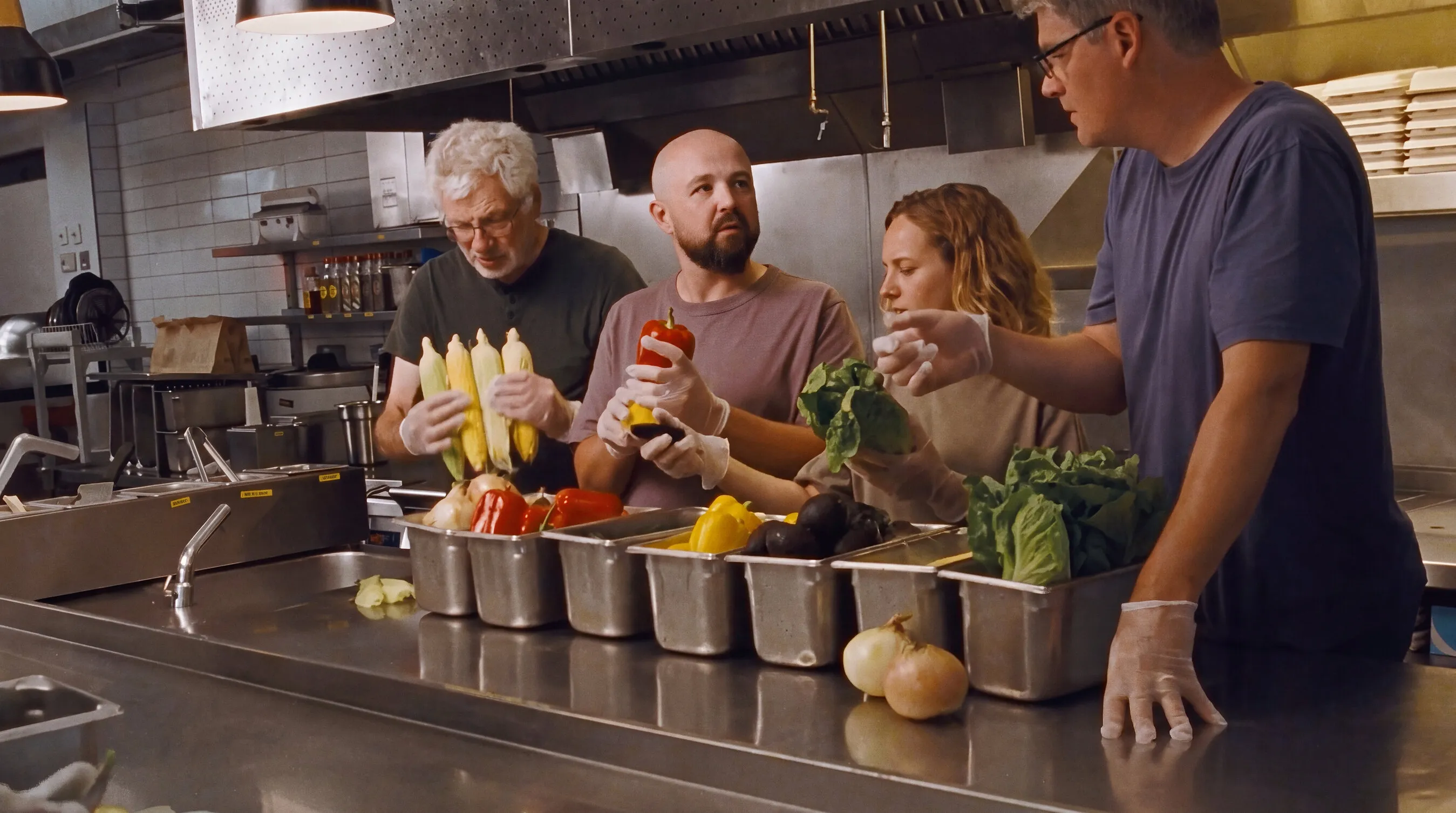 Four people preparing vegetables in a commercial kitchen.