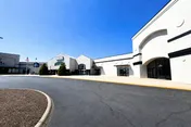 Exterior of a shopping center with storefronts, driveway and clear blue sky.