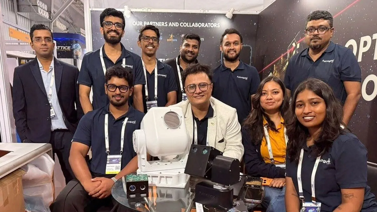 Nine people pose behind satellite equipment at an exhibition booth.
