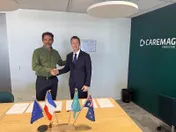 Two men shake hands beside a table with EU, French, Kazakh and Australian flags.