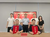 Two men hold red contract folders with six colleagues at a signing ceremony.