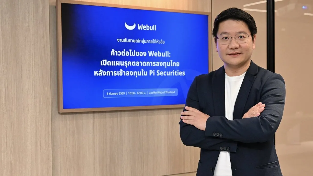 Man standing beside a screen displaying the Webull logo and Thai-language investment presentation.