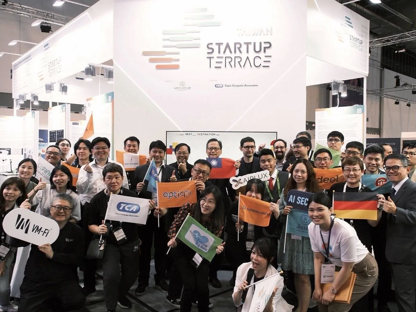 Group of attendees holding company signs and flags at the Startup Terrace exhibition booth.