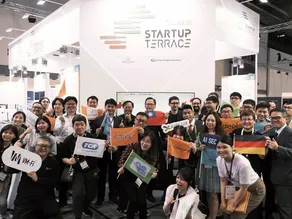 Group of attendees holding company signs and flags at the Startup Terrace exhibition booth.