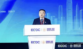 Man speaking at an ECDC and IDEE·SZ branded podium before a blue city skyline backdrop.