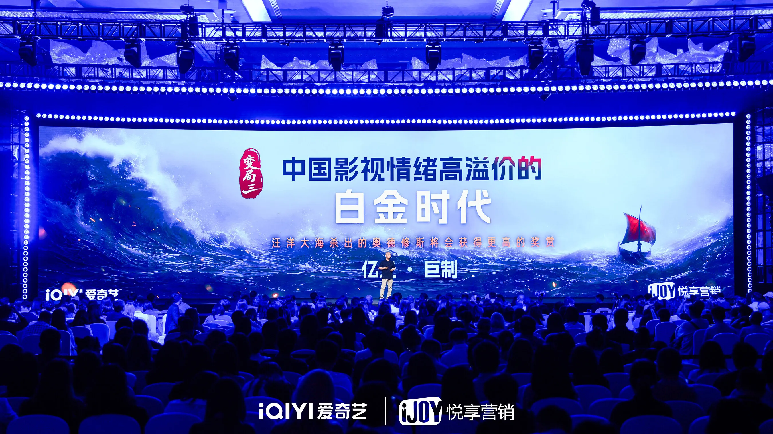 A speaker addresses an audience before a large screen showing ocean waves and a Viking ship.