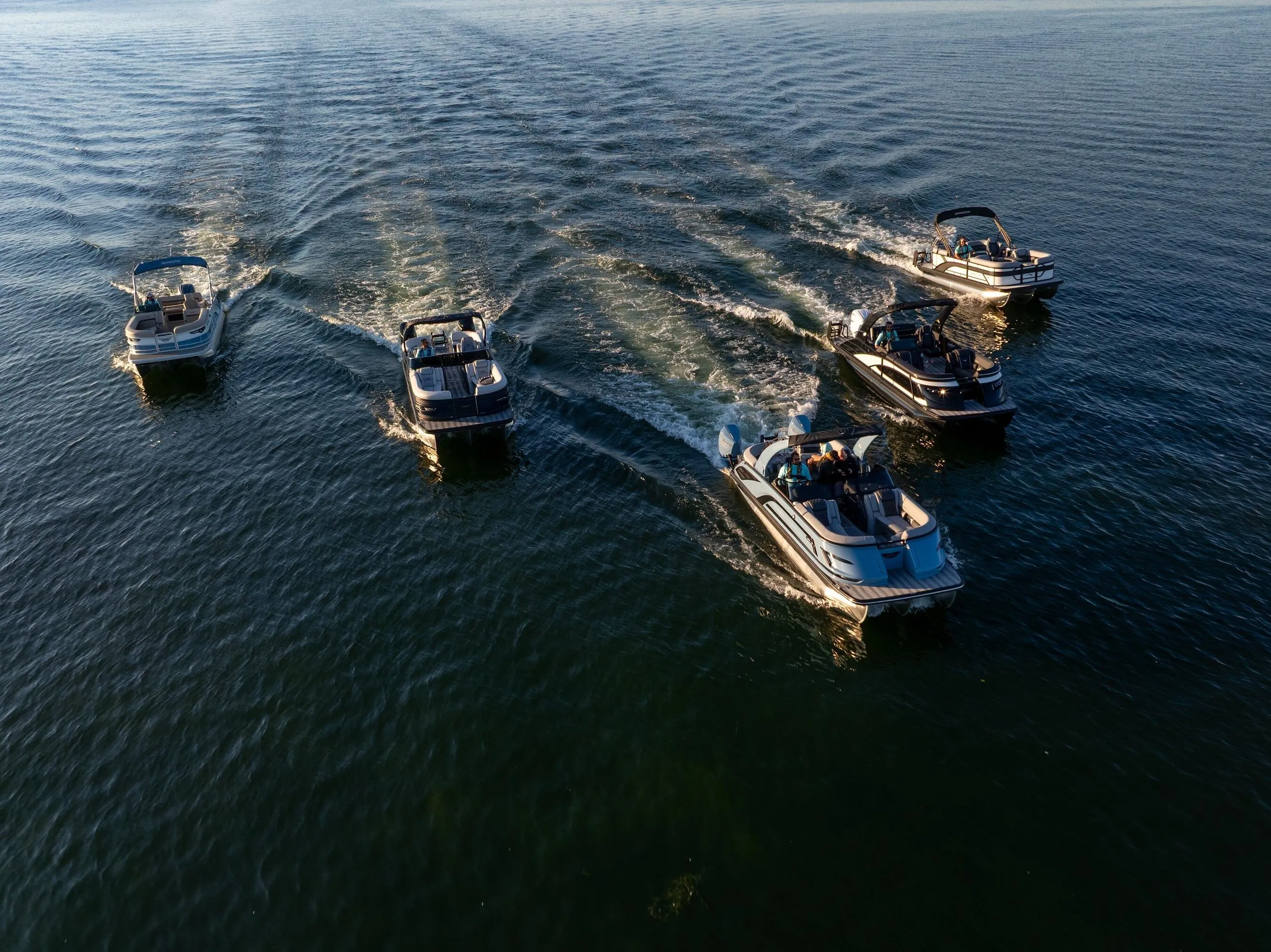 Five pontoon boats cruising across open water in formation.