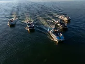 Five pontoon boats cruising across open water in formation.