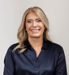 Carolina Dybeck Happe, smiling, in a dark blue blouse against a plain light grey background.