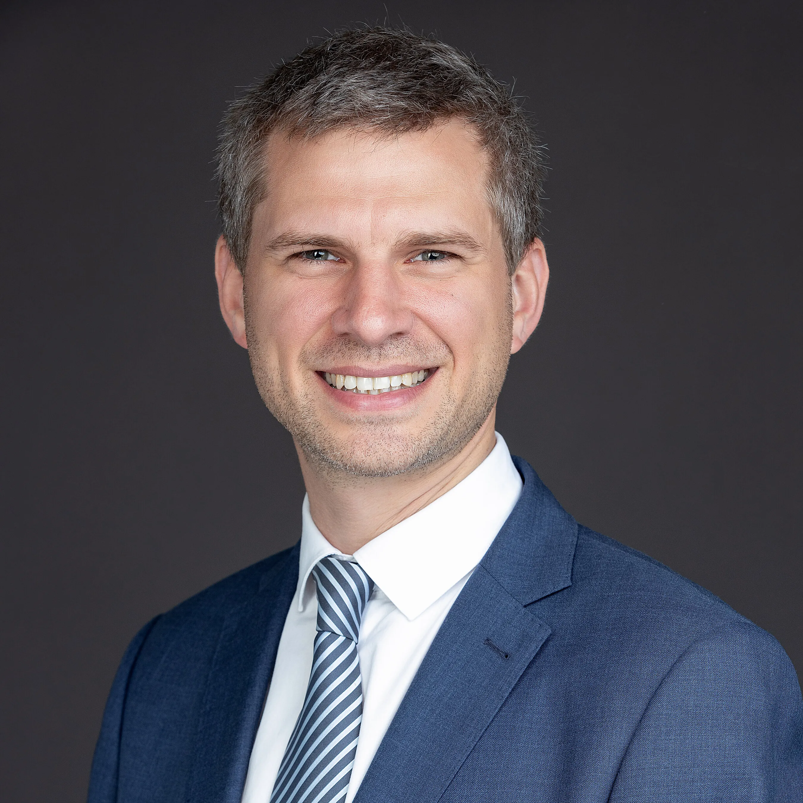 Edouard Wenseleers smiling in a blue suit and striped tie against a dark background.