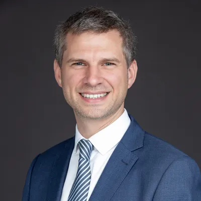 Edouard Wenseleers smiling in a blue suit and striped tie against a dark background.