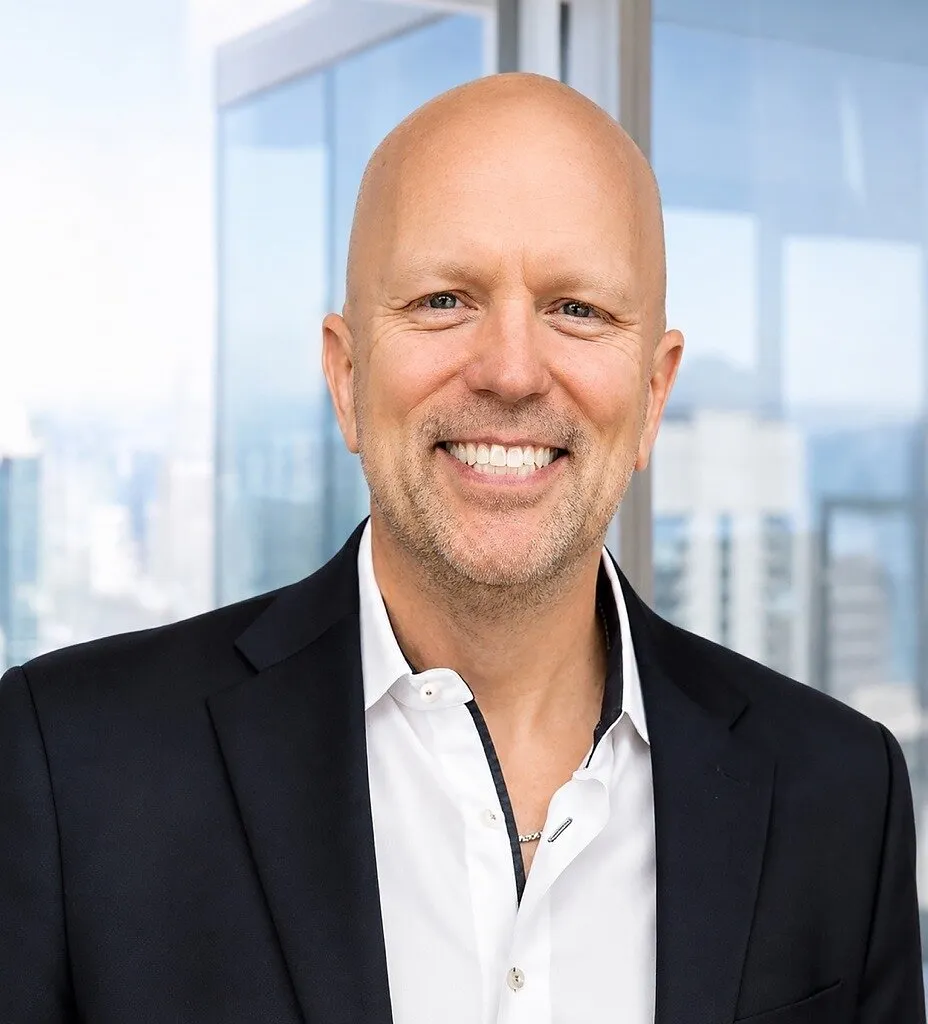Smiling bald man in a black blazer and white shirt in front of glass windows