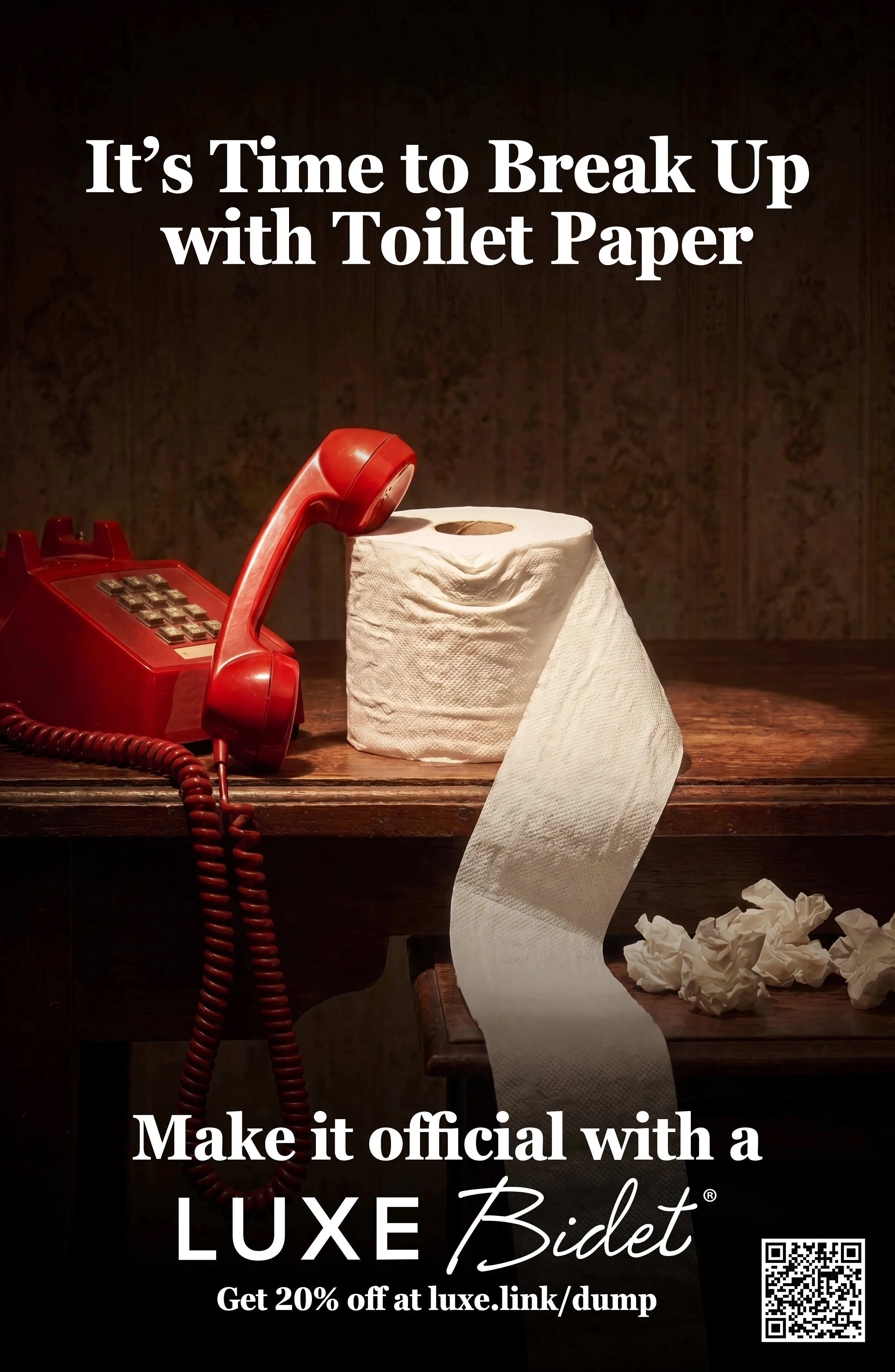 A red telephone beside a roll of toilet paper on a wooden table.