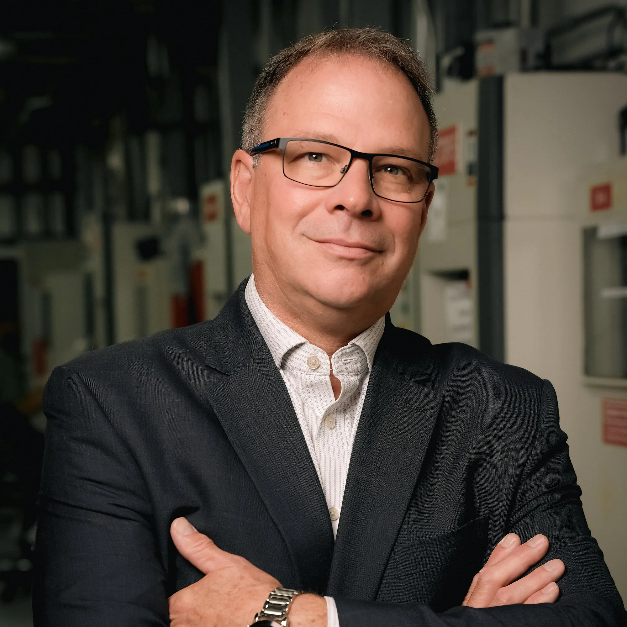 Don Garrison in glasses and a dark suit jacket, standing with arms crossed in an industrial setting.