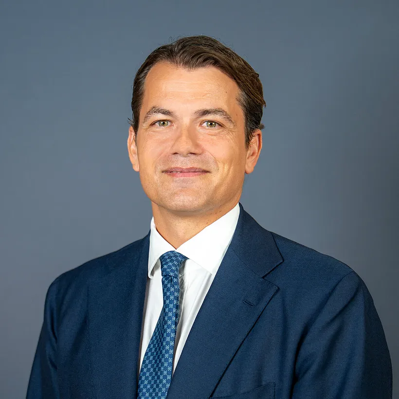 David Krap in a navy suit and patterned blue tie against a gray background