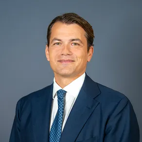 David Krap in a navy suit and patterned blue tie against a gray background
