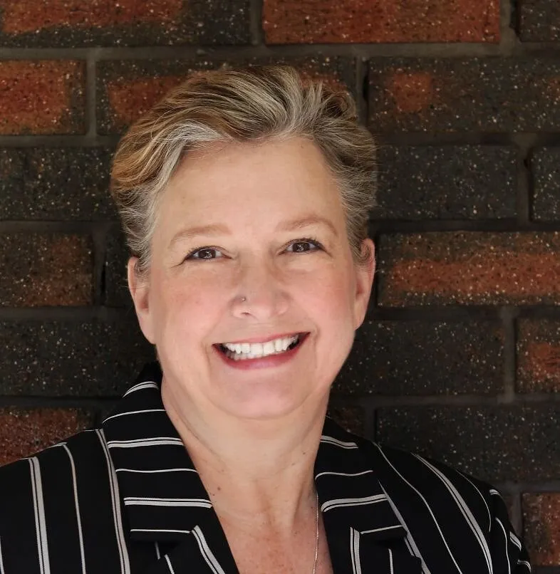 Leslie Jemiolo smiling in a black striped jacket against a brick wall.