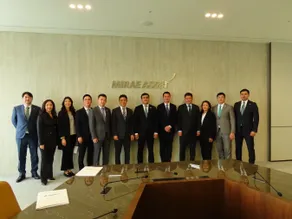 Eleven businesspeople standing before a Mirae Asset wall sign in a conference room.