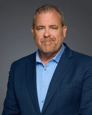 Jason Bradt in a blue blazer and light blue shirt against a gray background.