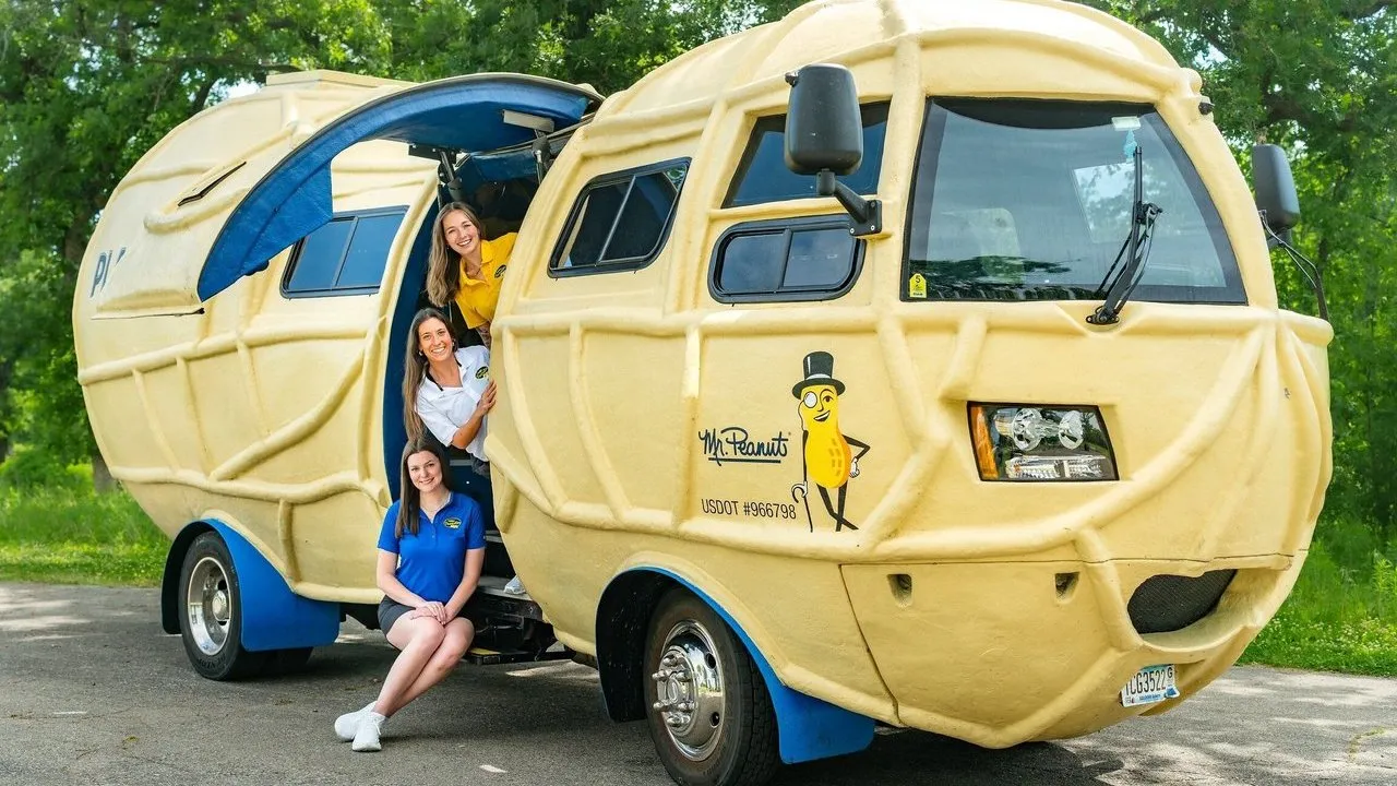 Three women beside and inside a Mr. Peanut-shaped promotional vehicle.