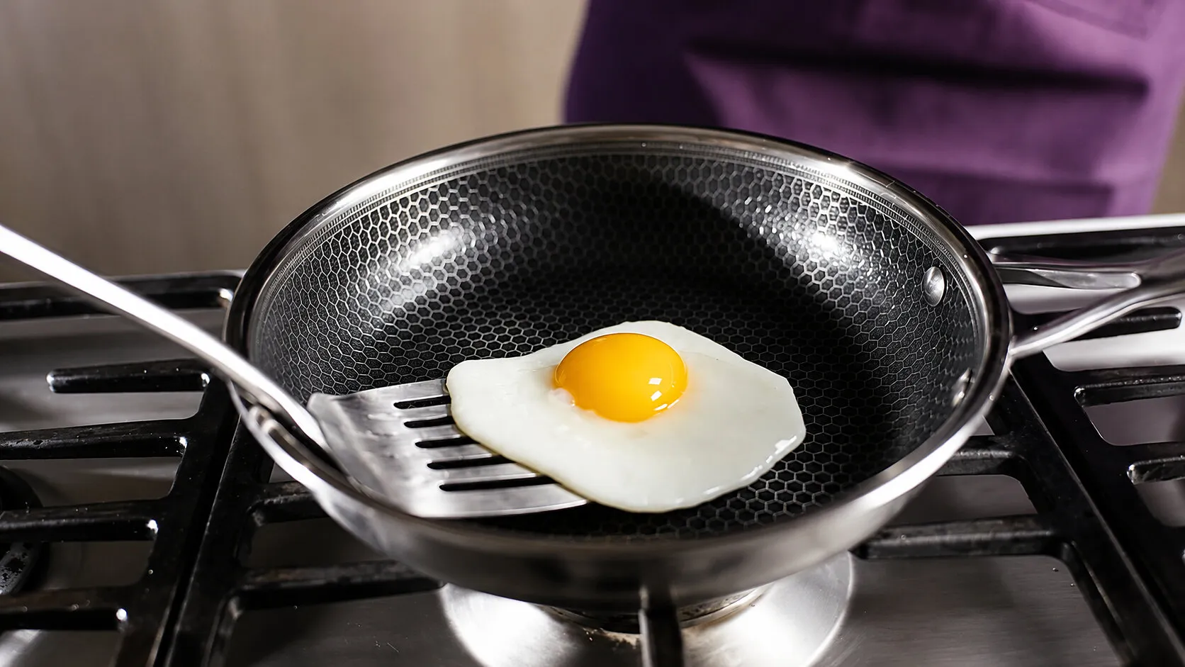 A sunny-side-up egg in a frying pan on a stovetop, with a spatula underneath.