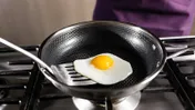 A sunny-side-up egg in a frying pan on a stovetop, with a spatula underneath.