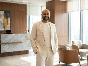 Rahul Gupta standing in a modern office reception area, wearing a cream suit.