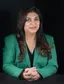 Shweta Rajpal Kohli in a green blazer, seated with hands clasped against a black background.