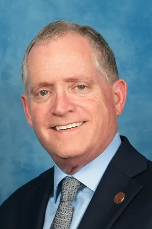 Neil H-Fishman in a suit and tie against a blue background.