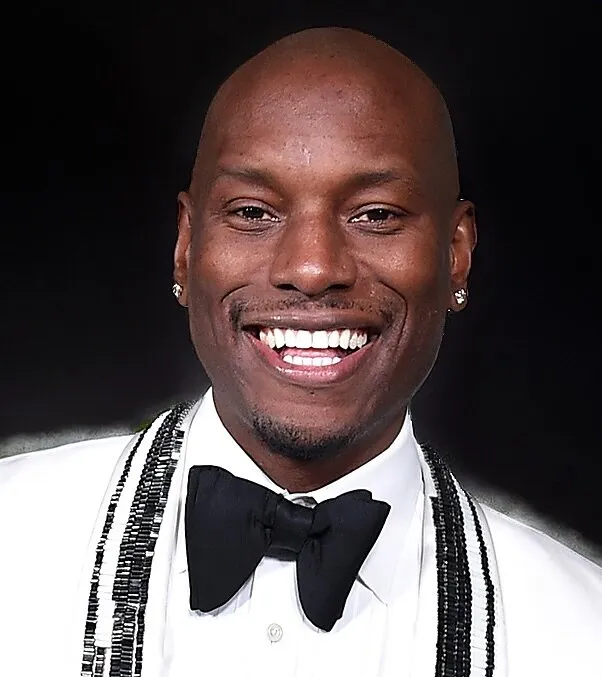 Tyrese Gibson smiling in a white tuxedo jacket with black trim and a black bow tie.