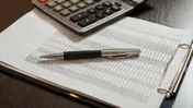Calculator and pen resting on a printed spreadsheet beside eyeglasses.