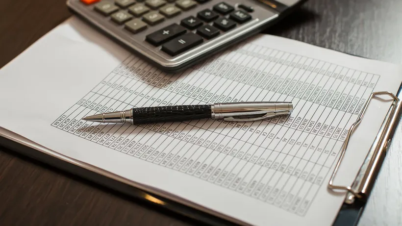 Calculator and pen resting on a printed spreadsheet beside eyeglasses.
