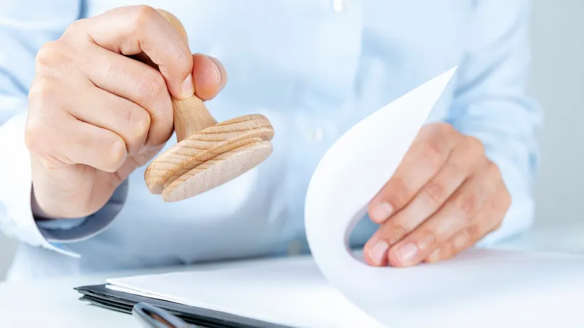 Close-up of hands holding a wooden stamp above papers on a desk.