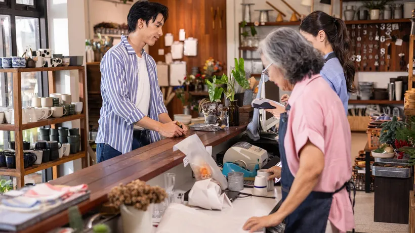 Customer pays at a shop counter while two people work behind it.
