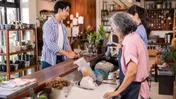 Customer pays at a shop counter while two people work behind it.