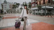 Woman pulling a suitcase and carrying shopping bags on a wet city street.