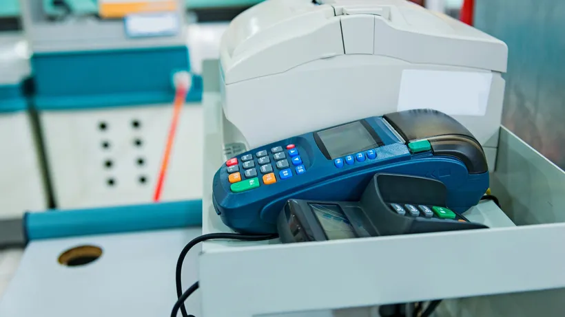 Card payment terminal beside a cash register at a retail checkout counter.