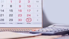 Calendar with a red-circled date beside a calculator and paperwork.