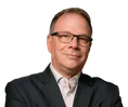 Don Garrison in glasses and a dark suit jacket, standing with arms crossed in an industrial setting.