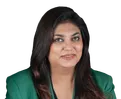 Shweta Rajpal Kohli in a green blazer, seated with hands clasped against a black background.