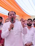 A person in a white shirt speaks into a microphone beneath orange and white drapes.