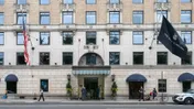 The entrance of The Ritz-Carlton New York, Central Park, with hotel staff at the door, luggage trolleys and a Ritz-Carlton flag