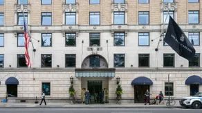The entrance of The Ritz-Carlton New York, Central Park, with hotel staff at the door, luggage trolleys and a Ritz-Carlton flag