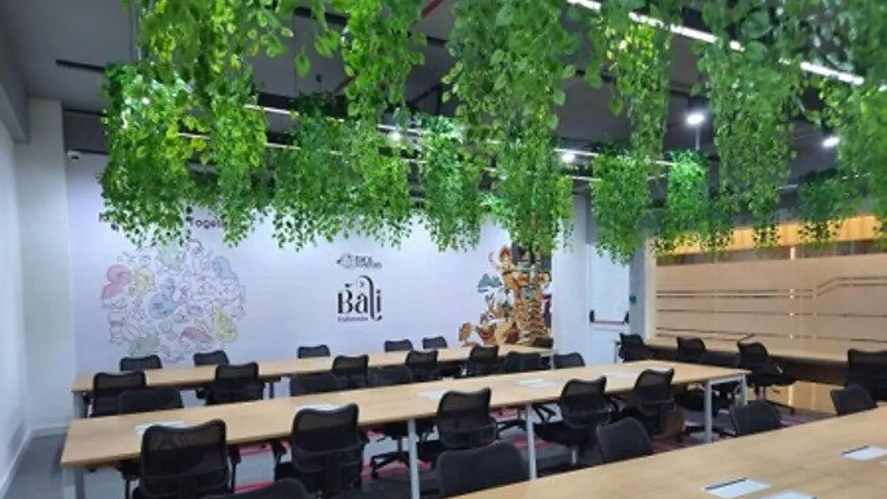 Office training room with long desks, black chairs, hanging plants and Bali-themed wall art.